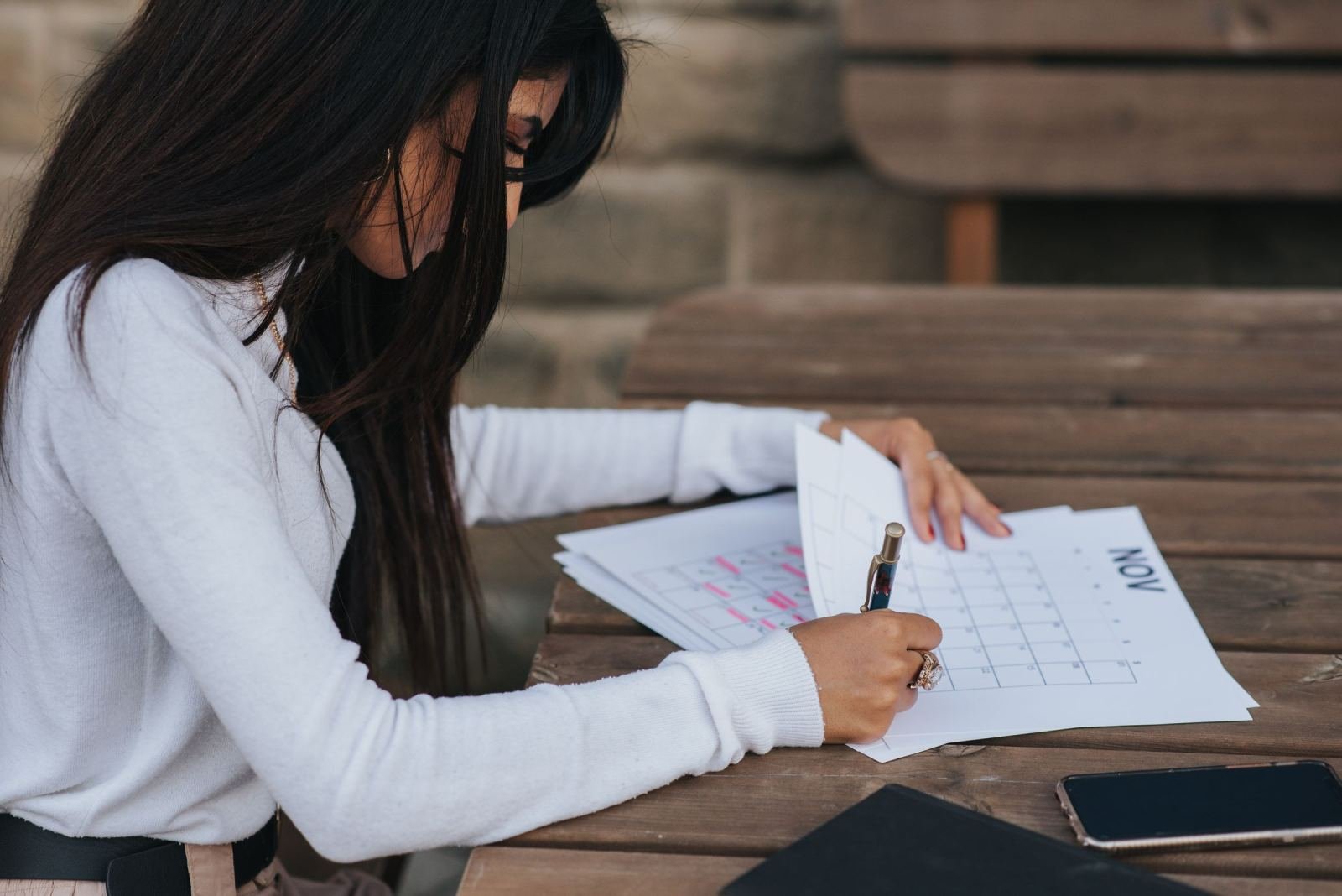 A woman writes on a printed calendar at a wooden table