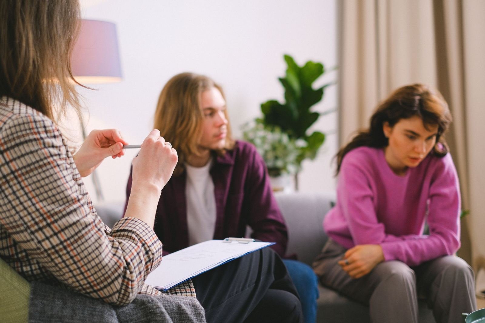 A counselor with a clipboard talks with a man and a woman on a sofa