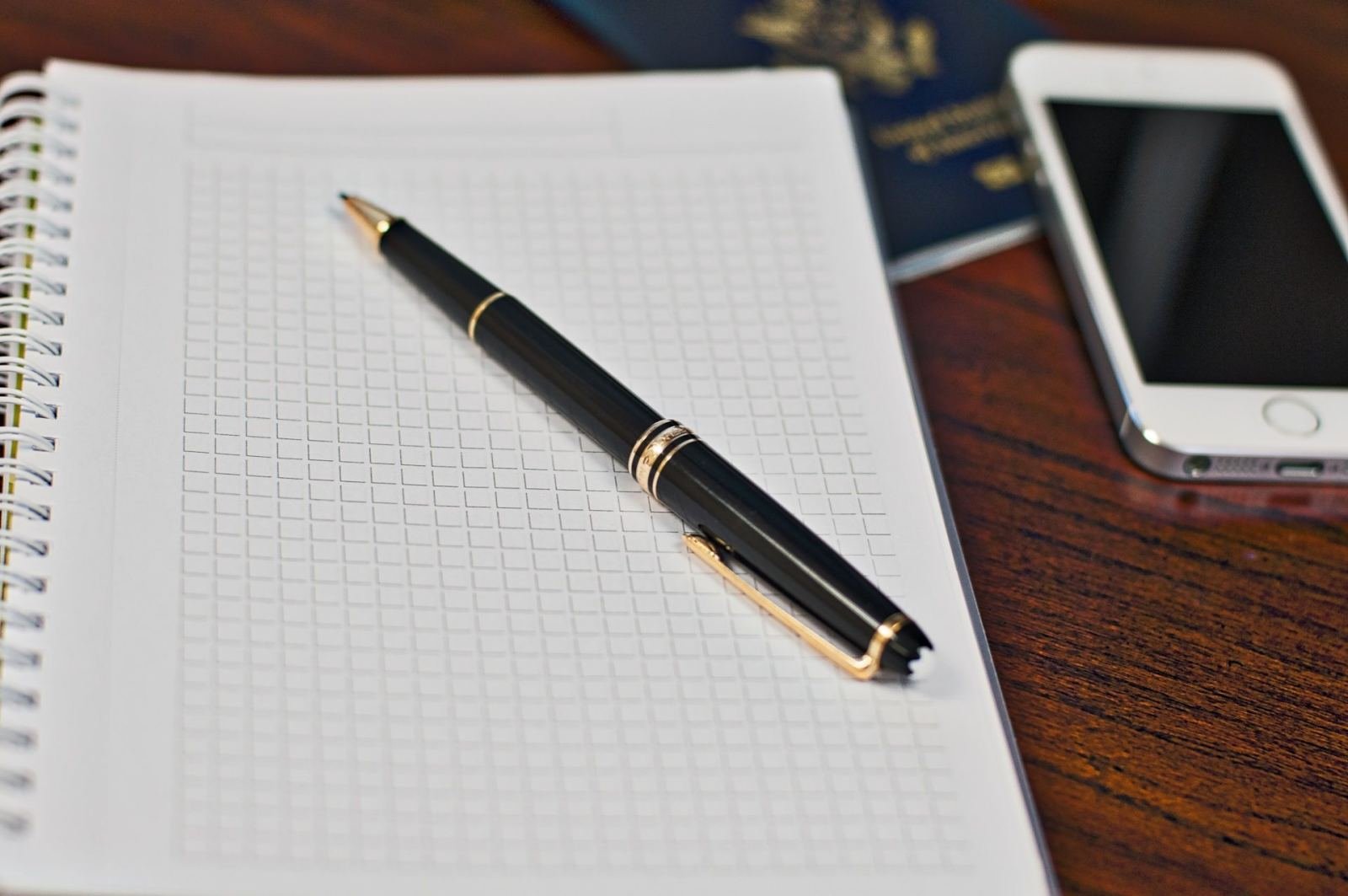 A black pen on a grid notebook next to a smartphone on a wooden desk