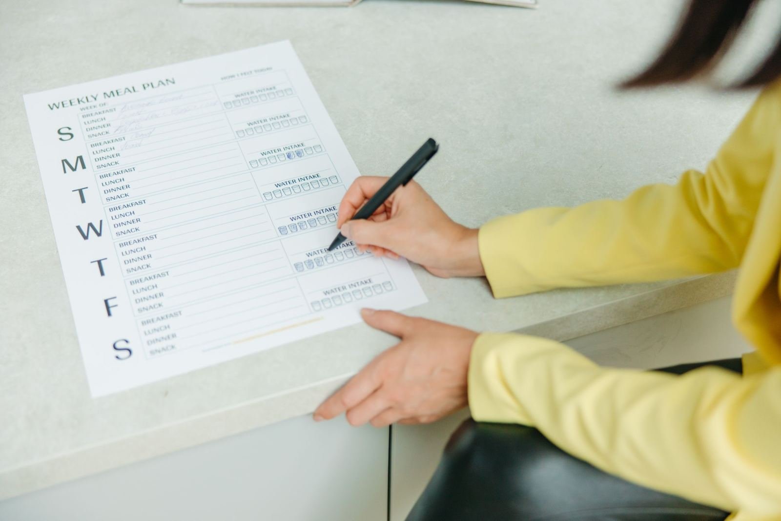 A person in a yellow shirt writes on a weekly meal plan document