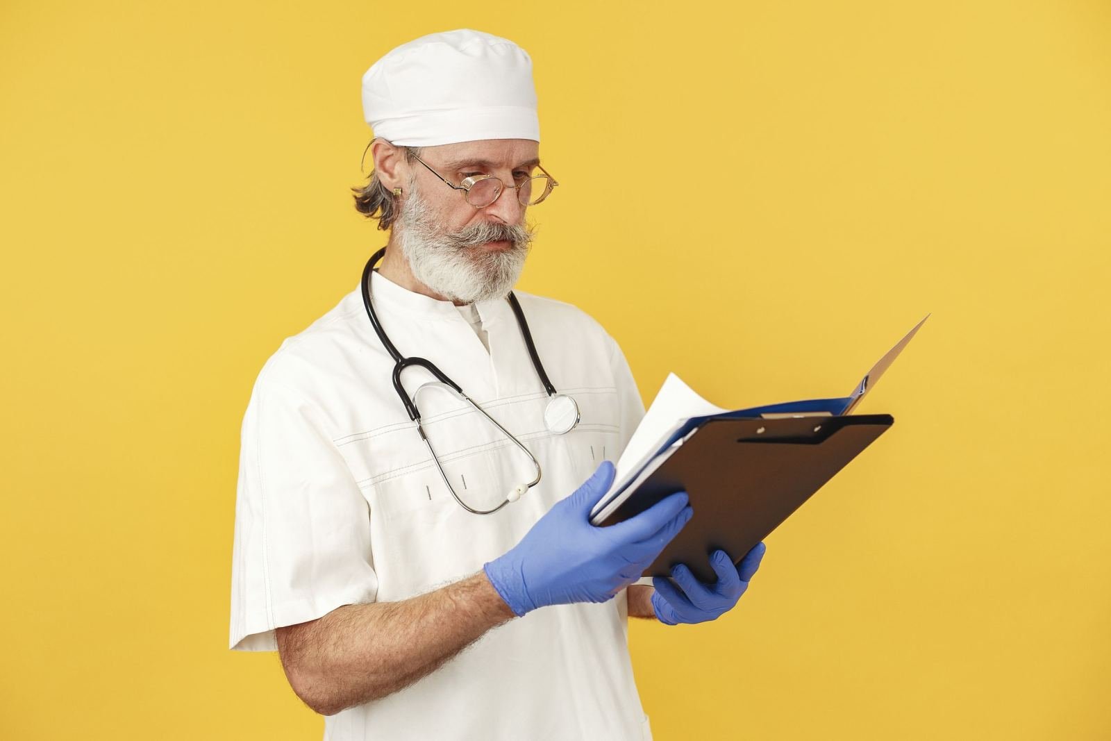 A clinician in a white coat and blue gloves reading a clipboard