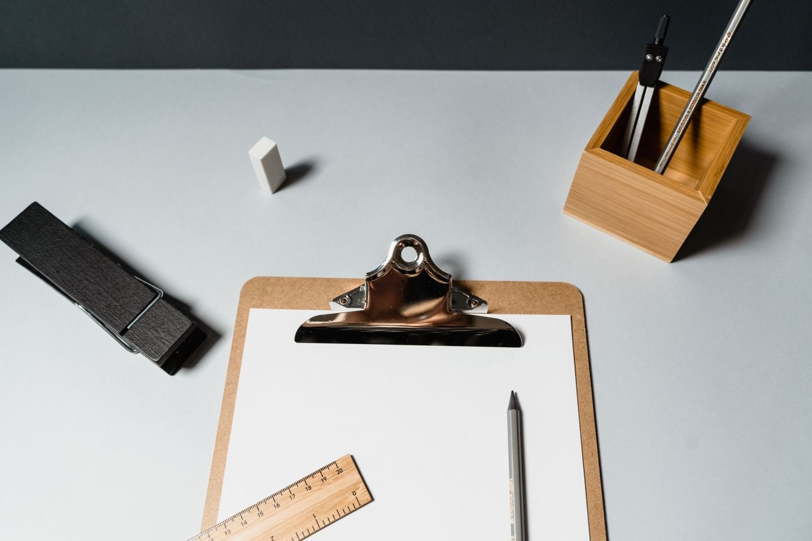 A blank clipboard, pencil, and ruler on a light gray desk