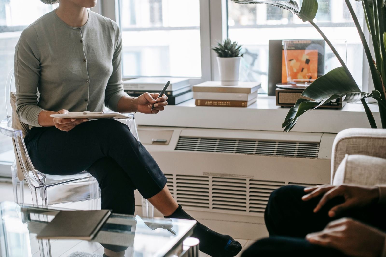 A professional with a clipboard sits in a clear chair talking to a client