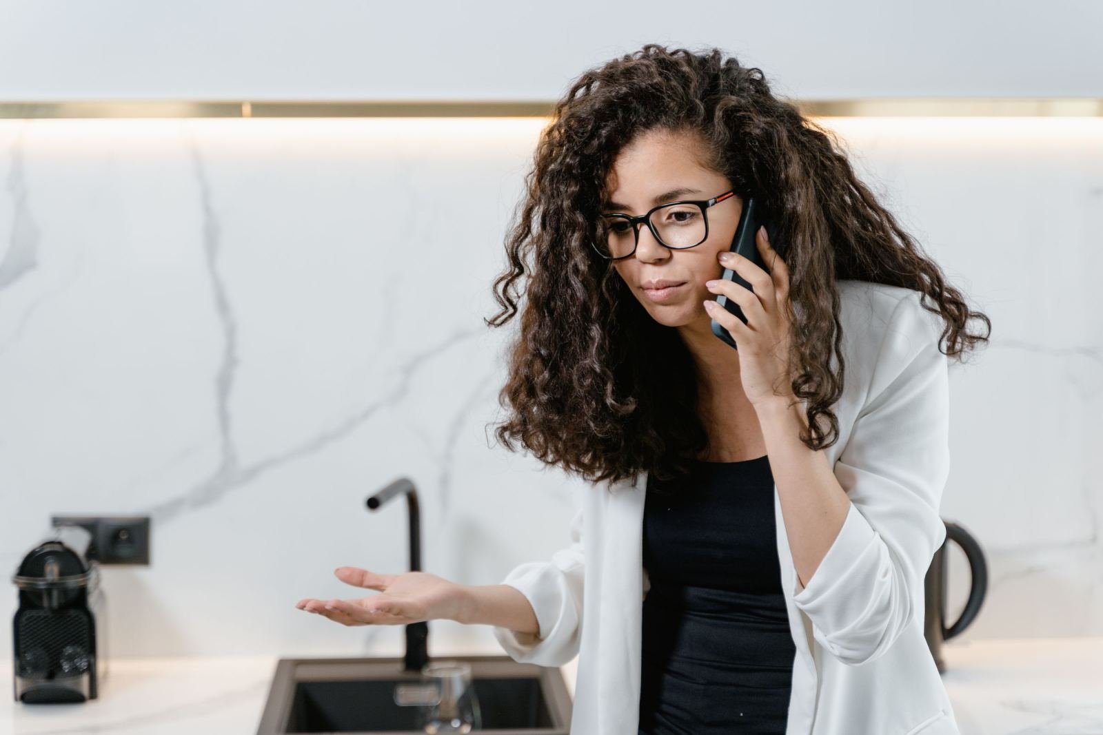 A woman with glasses talks on a mobile phone in a modern kitchen