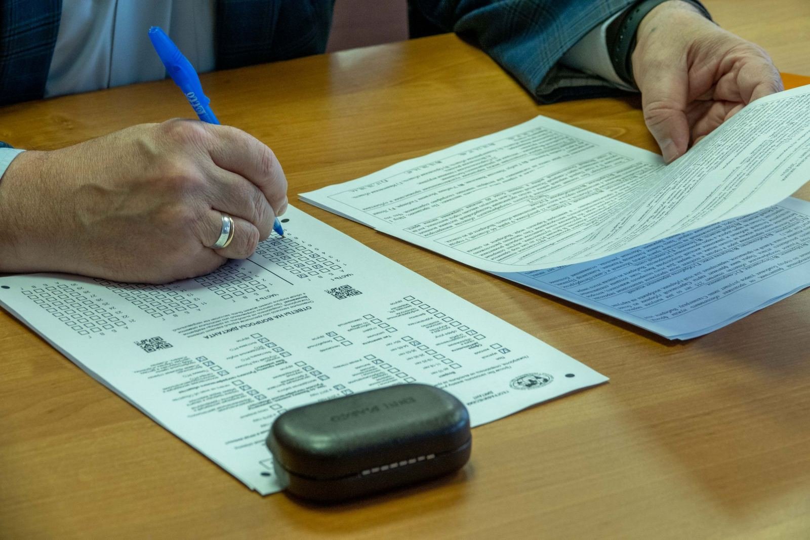Hands filling out a form with a blue pen on a wooden table
