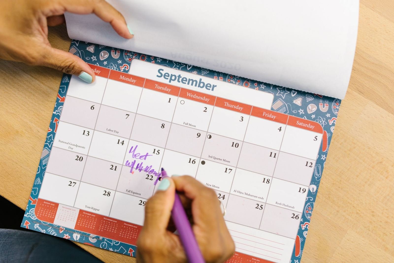 A person uses a purple marker to write a note on a September calendar