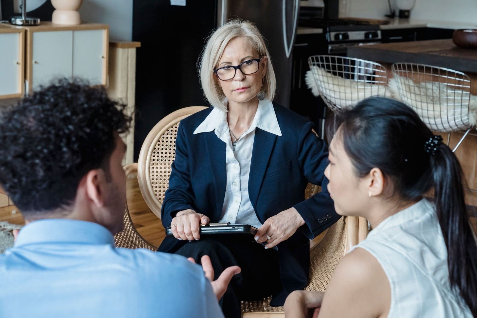 A professional woman in a blazer speaks with a man and woman in a bright room