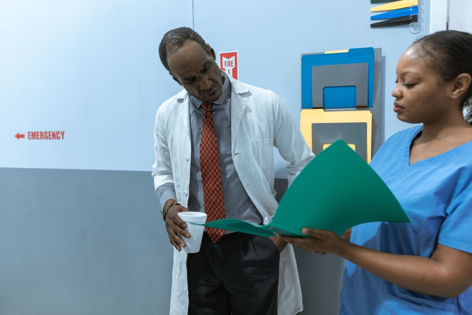 A doctor and a nurse in scrubs review a green folder together