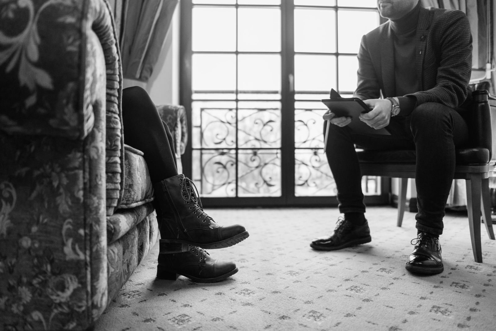 One person holds a notebook while sitting across from another in a room.