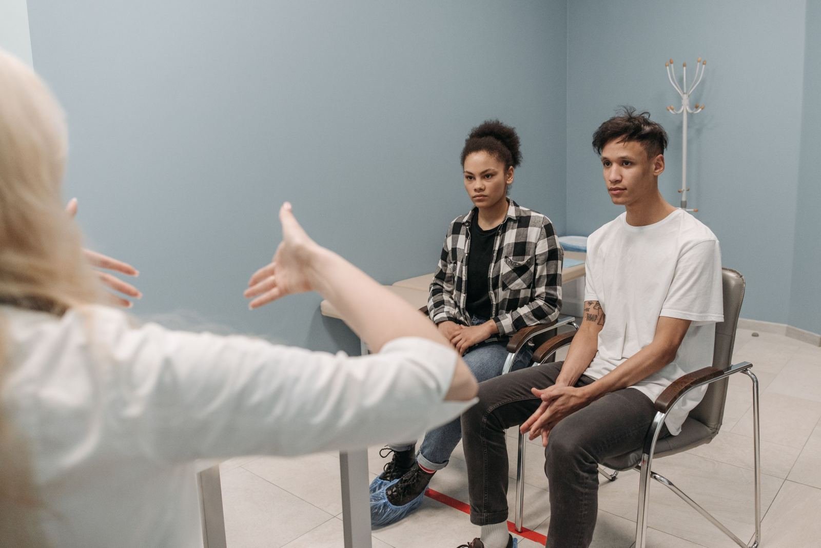 A counselor gestures while speaking to a young man and woman in a plain room