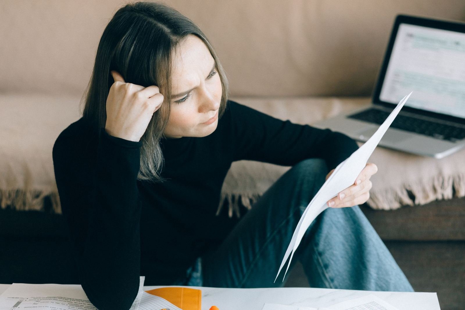 A woman sits on the floor leaning against a sofa while reviewing a document