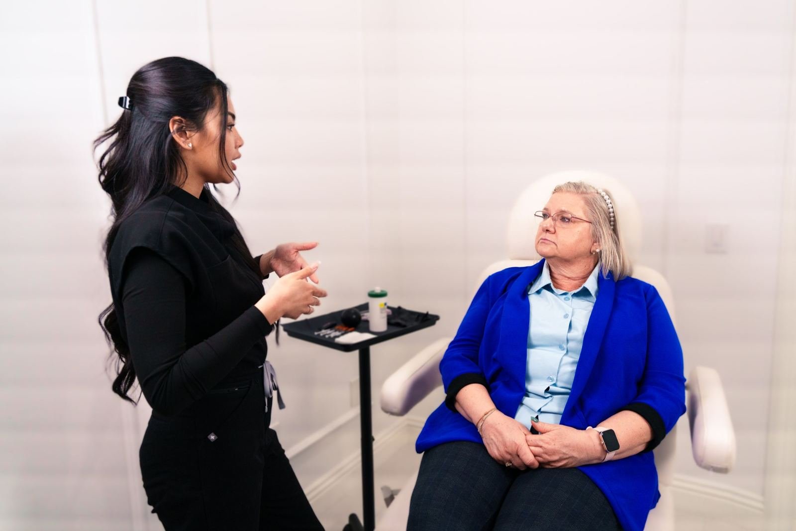 A care coordinator in black speaks with a patient sitting in a white medical chair