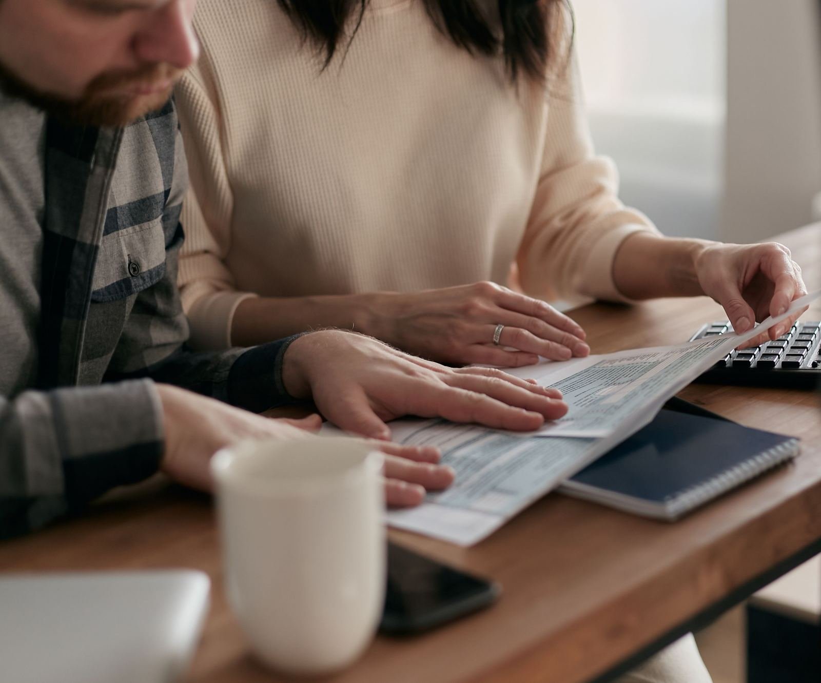 A man and a woman sit at a wooden table. They go over some paperwork together.
