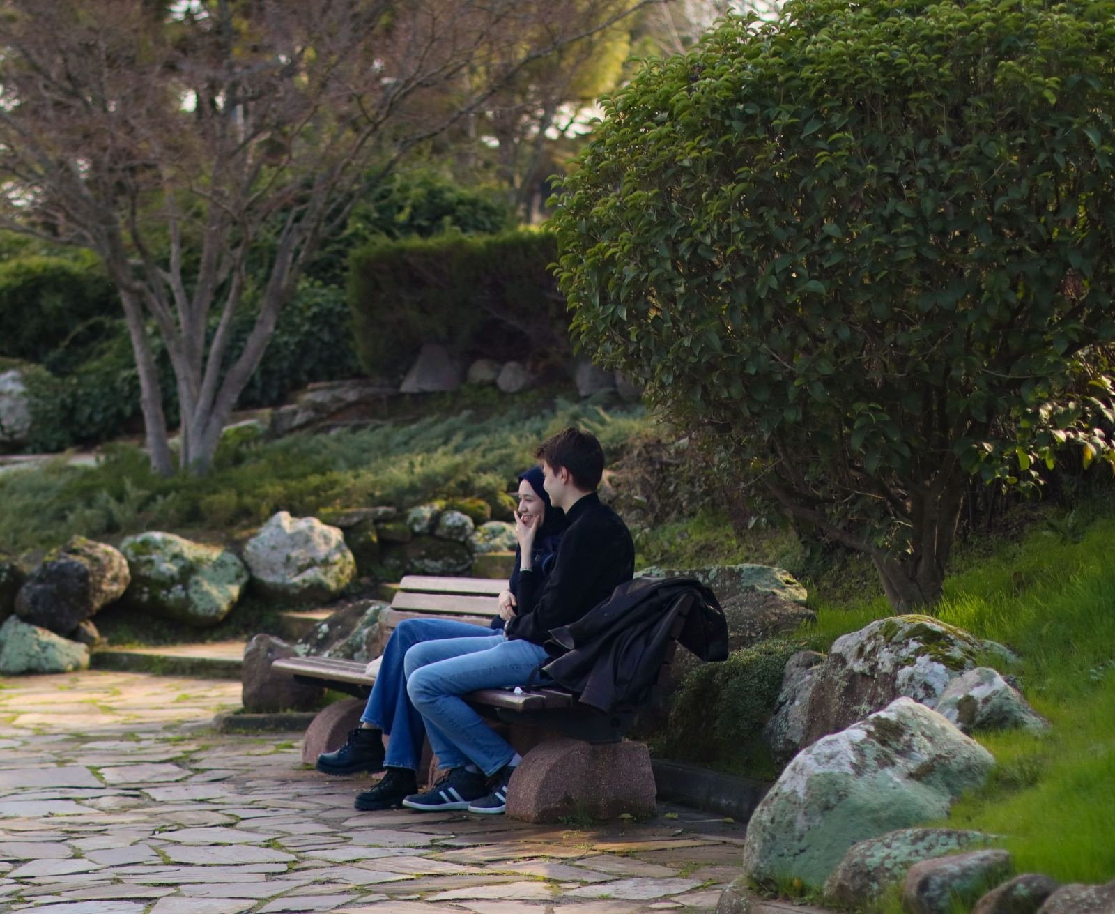 Two people sitting on a wooden park bench talking in a garden