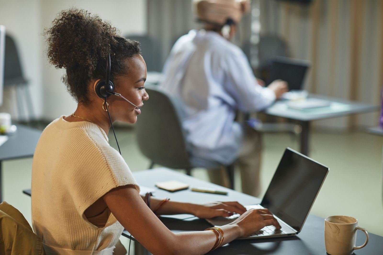 A woman with a headset types on a laptop in an office setting
