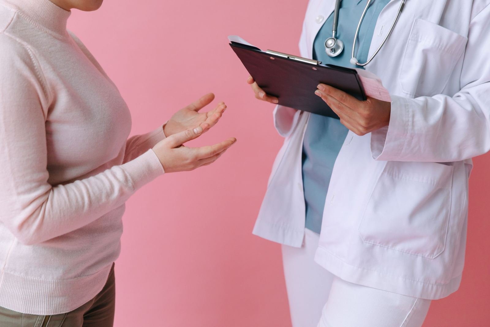 A person in a white sweater talks to a healthcare provider holding a clipboard