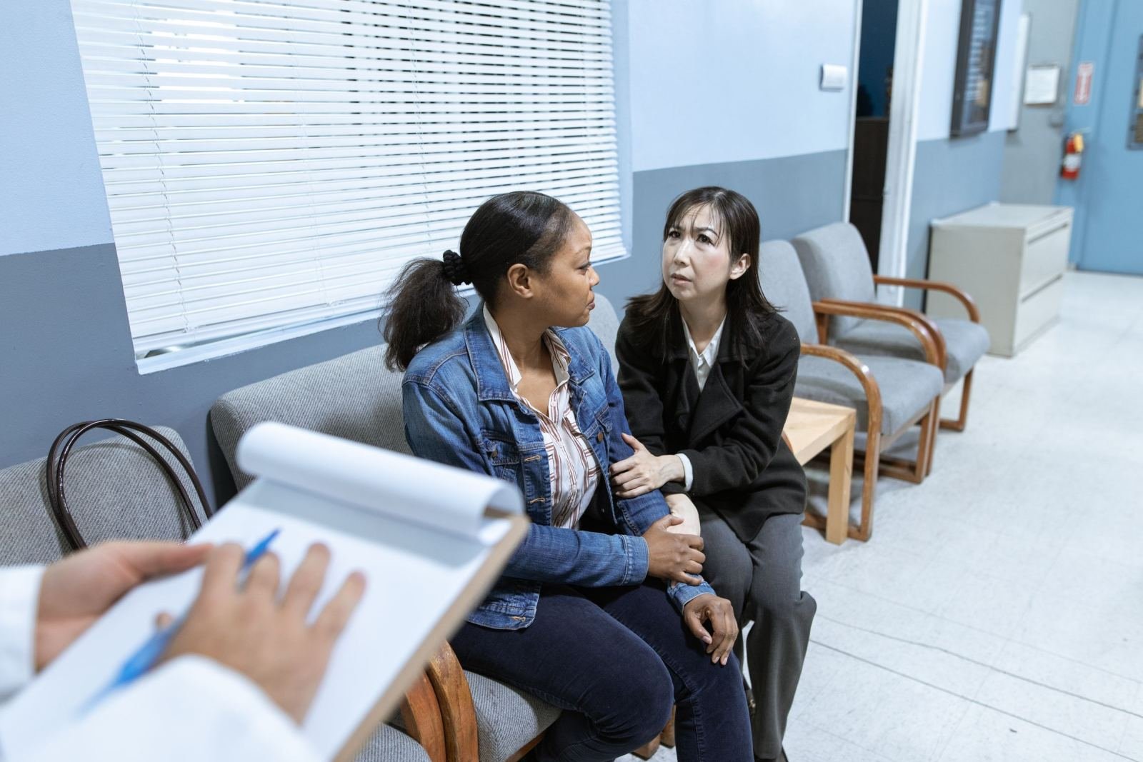A clinician with a clipboard sits with two women on a couch in an office.