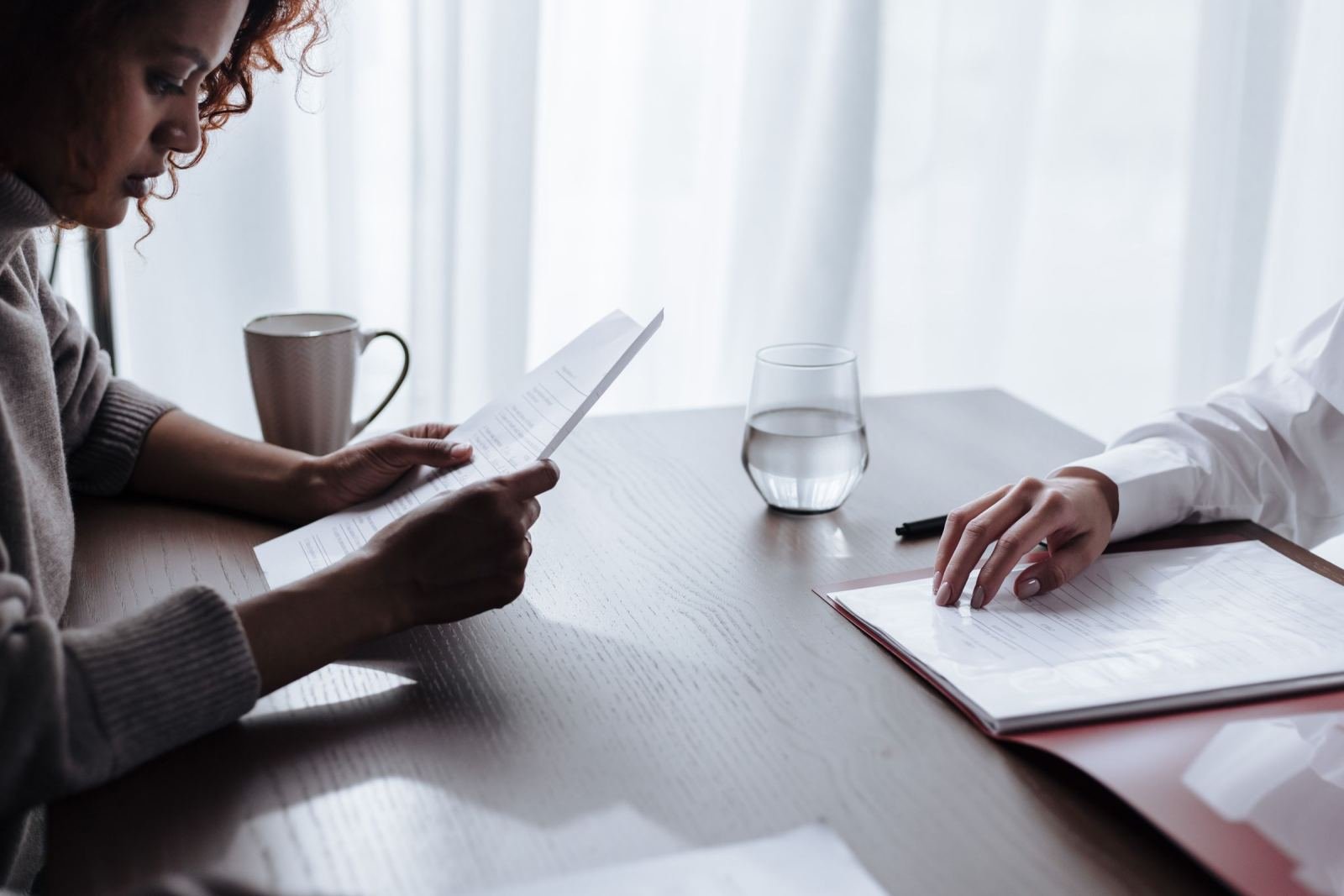 Two people review printed documents and a folder at a wooden table