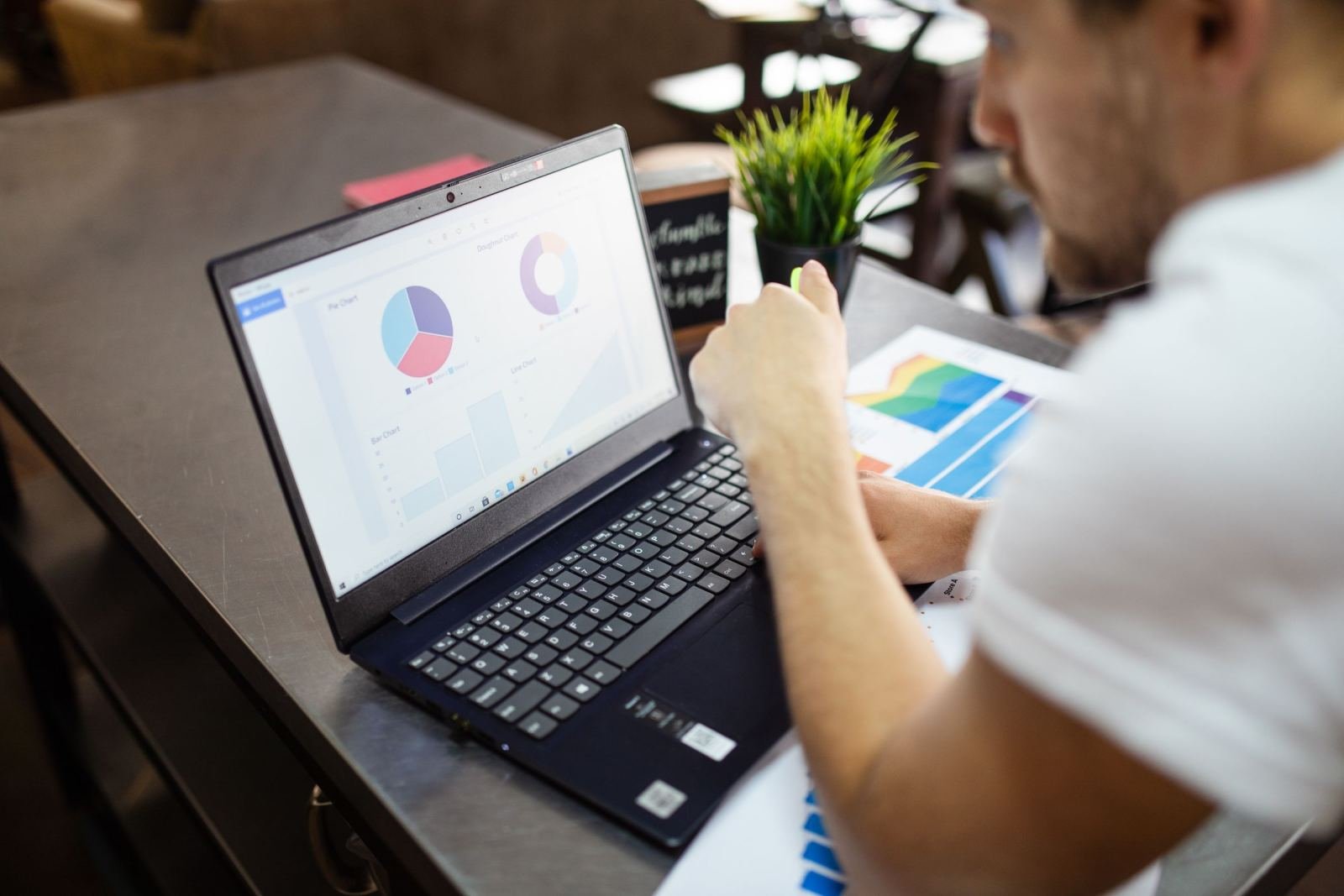 A man looks at data charts on a laptop and printed papers at a desk