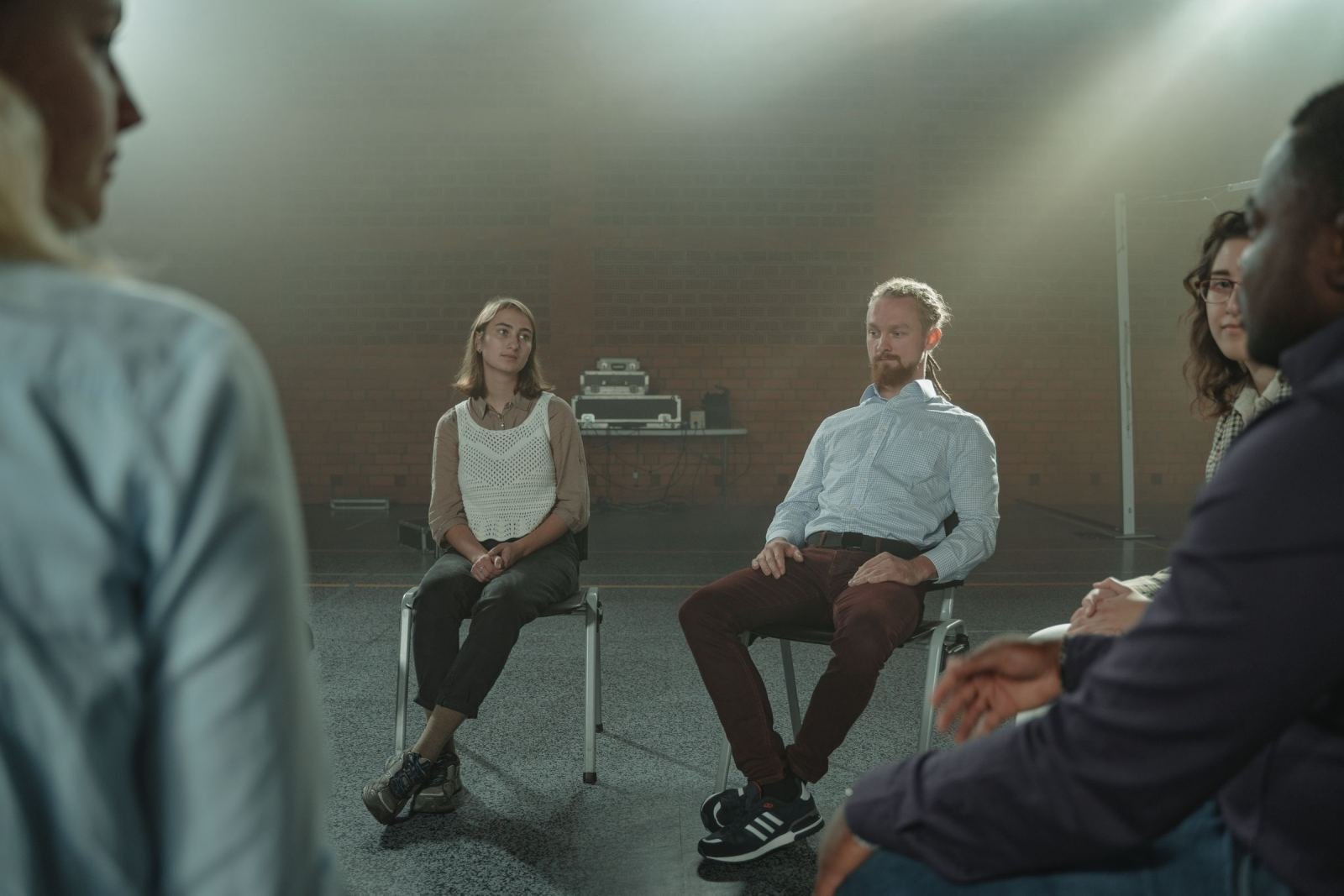 A group of adults sit in a circle for a support meeting in a dim room