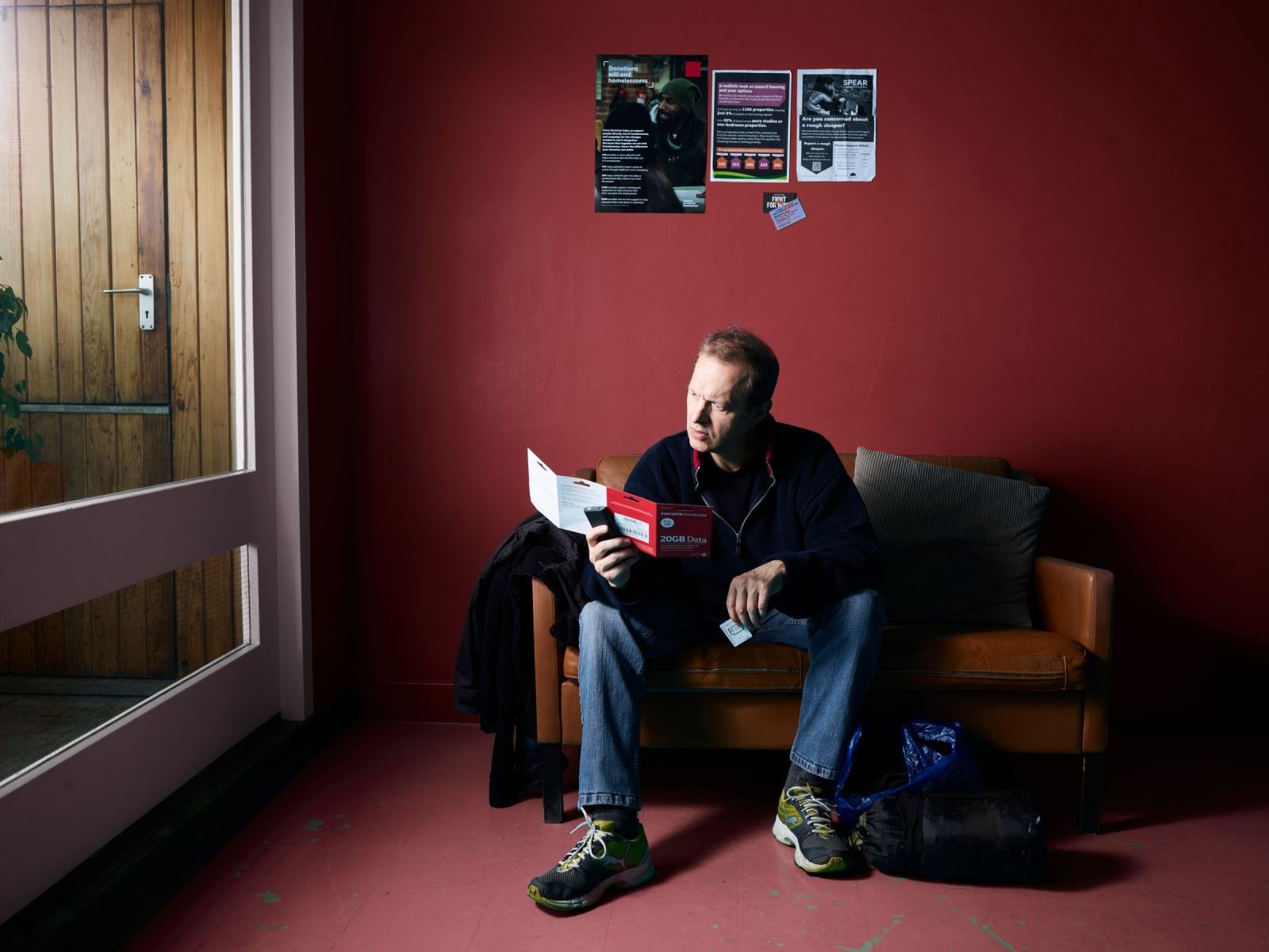 A man sitting on a leather sofa looks at a piece of paper and a smartphone
