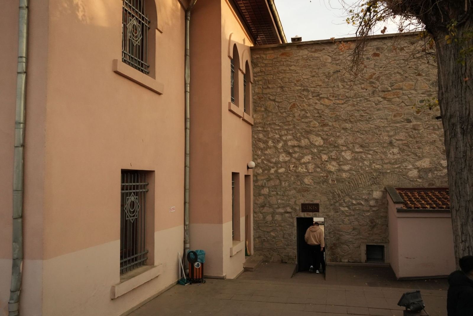 Someone steps through a door into a stone building beside a pink wall