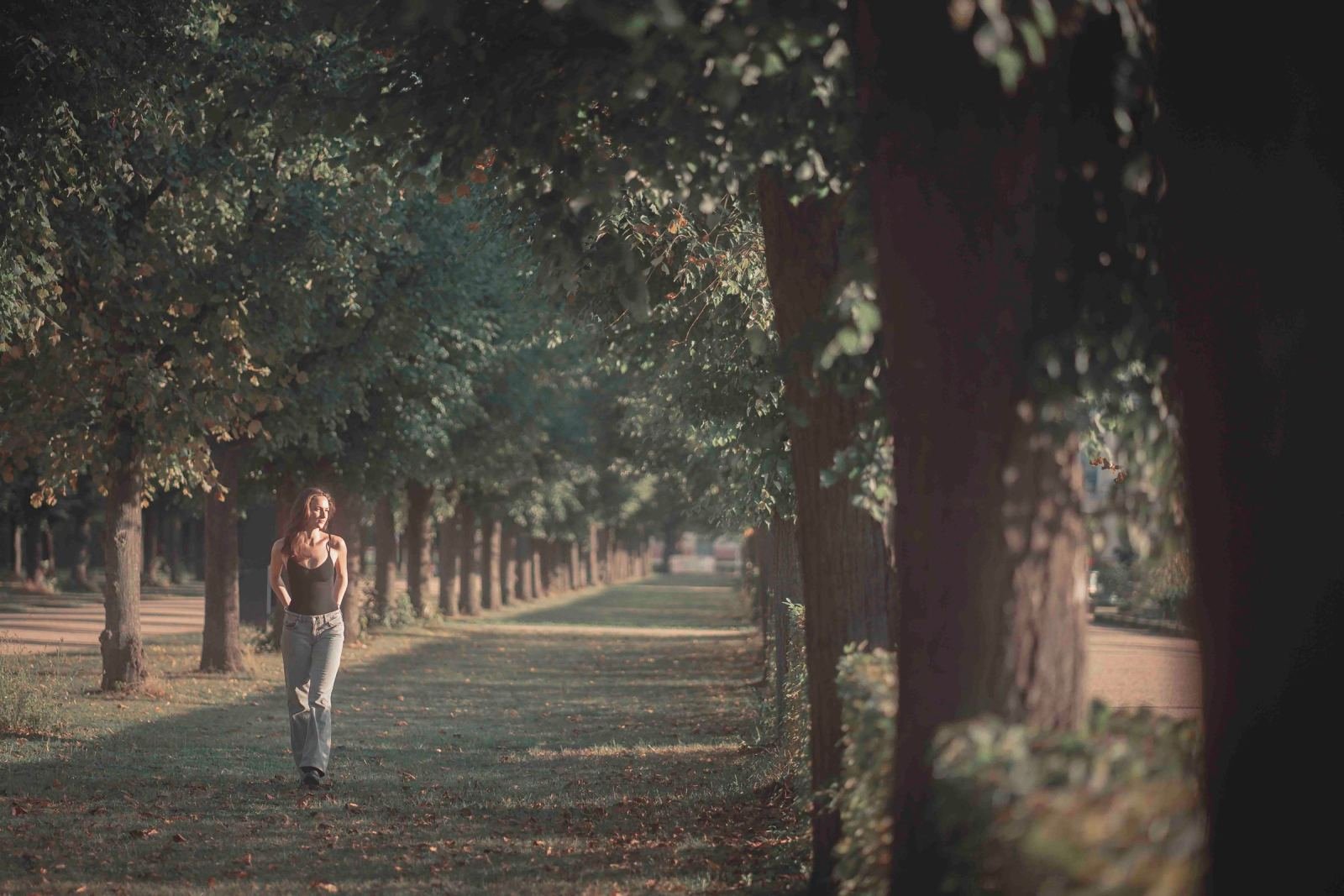 A woman walks along a grassy path lined with tall trees