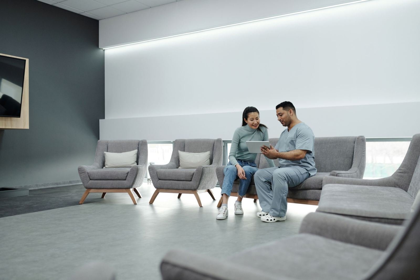 A man and woman share a tablet while sitting on a gray couch.
