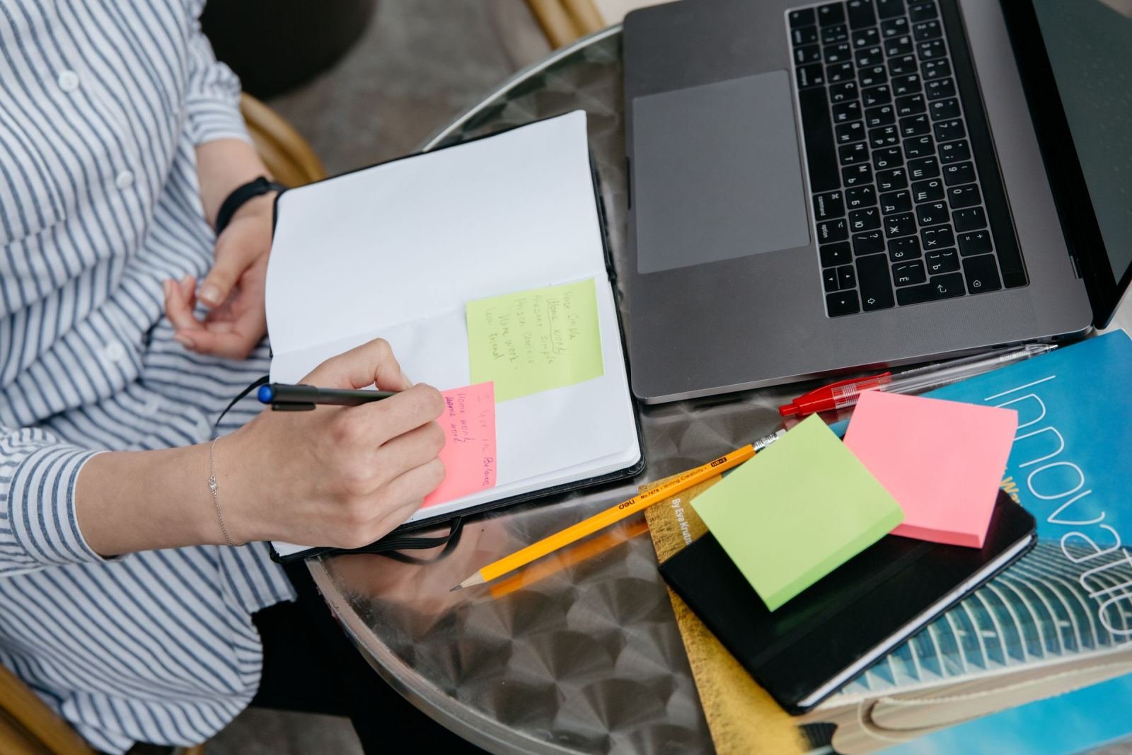A person writing in a notebook next to a laptop and sticky notes