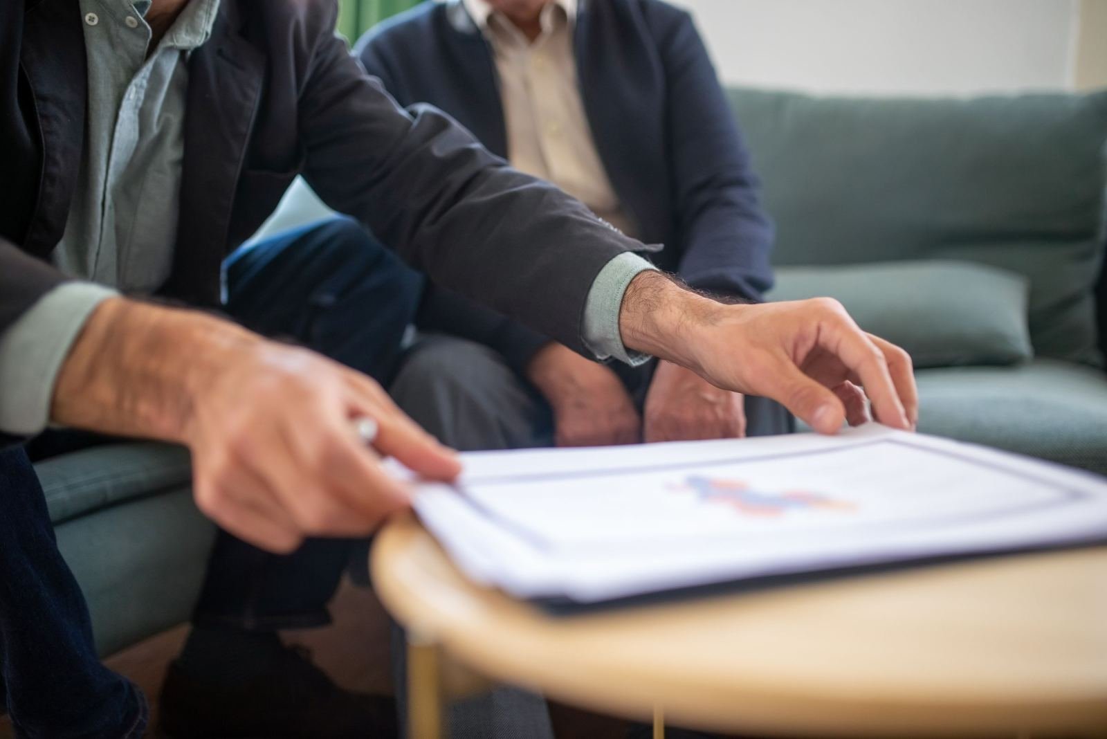 Two people in suits discuss a document with a chart on a wooden table