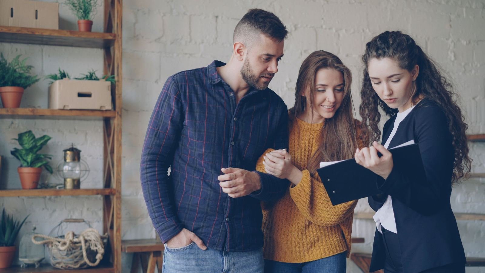 A man and a woman sit with a counselor who holds a clipboard and checks her notes.