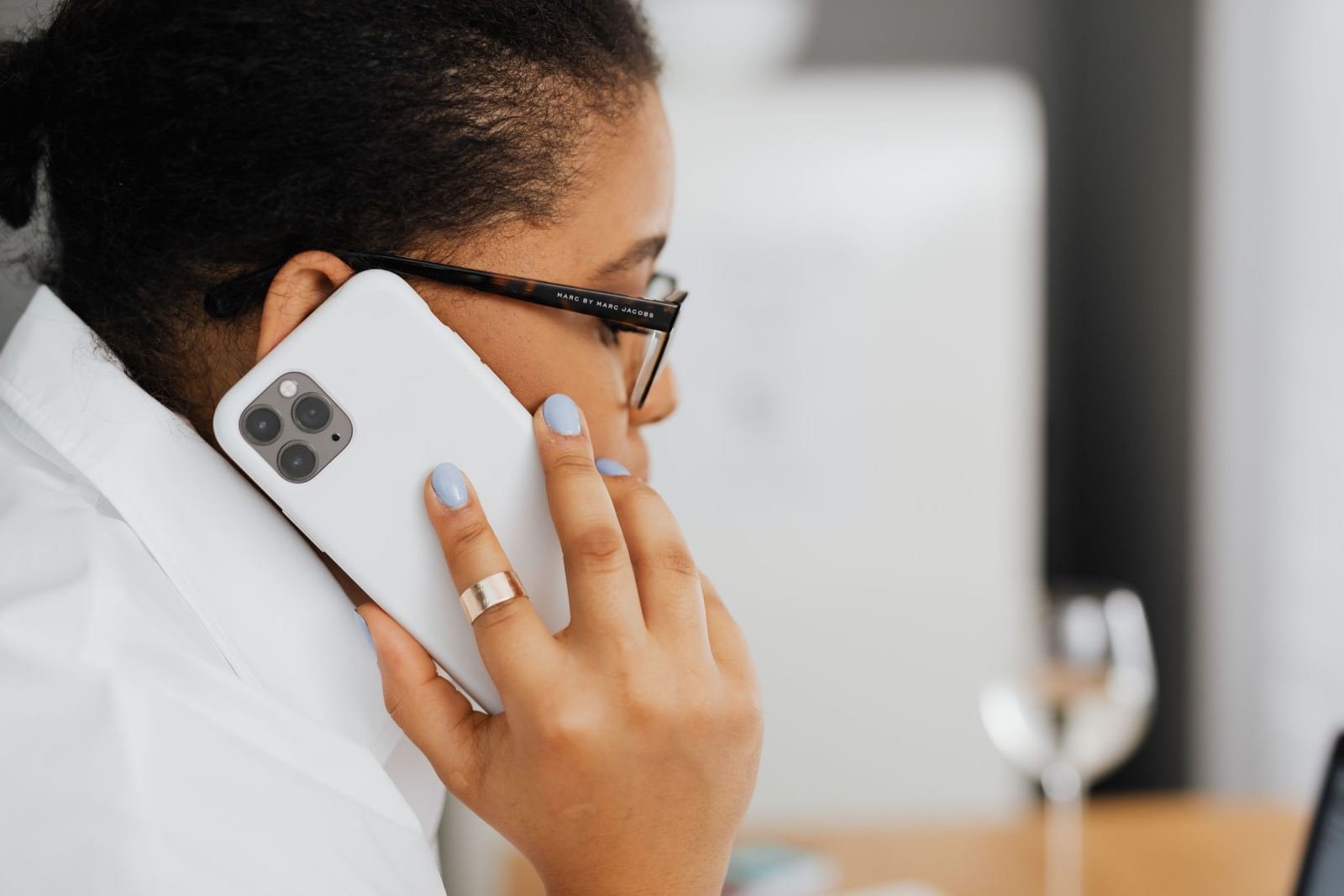 A person with glasses talks on a white smartphone