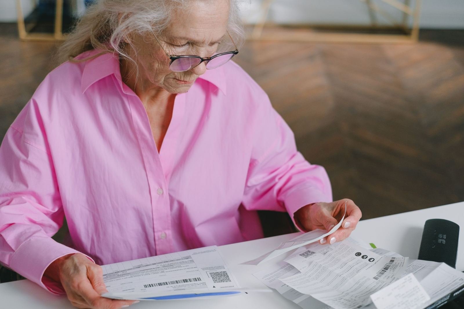 An older woman in a pink shirt reviews printed documents on a white table