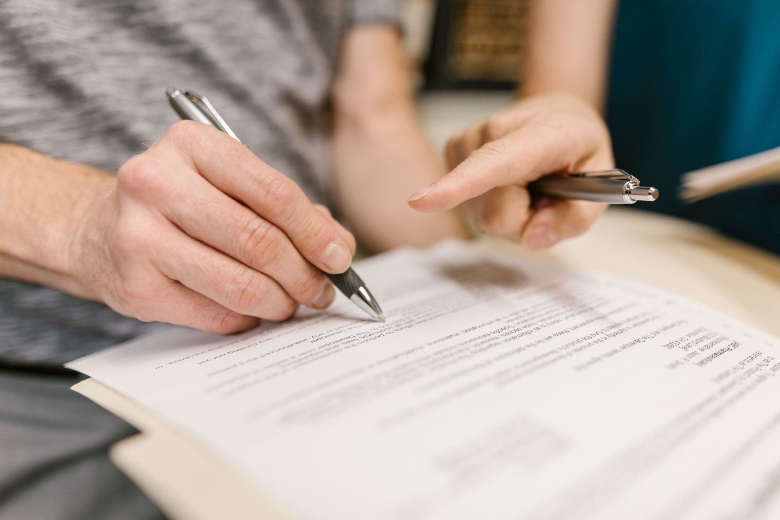 Two people fill out forms and sign them at a desk