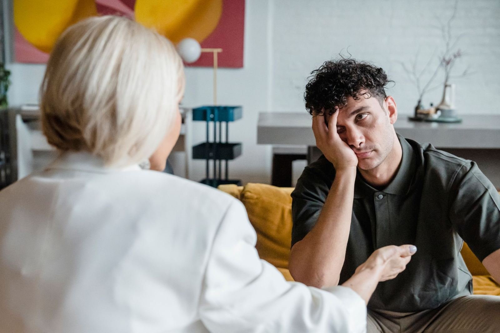 A man in a white blazer listens to a professional while resting his head on his hand.