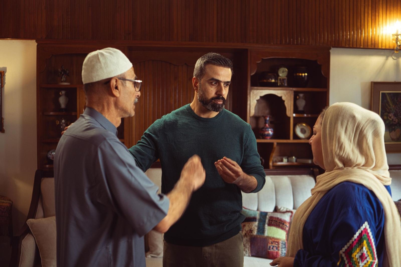 Three people in traditional and casual dress talk together in a living room