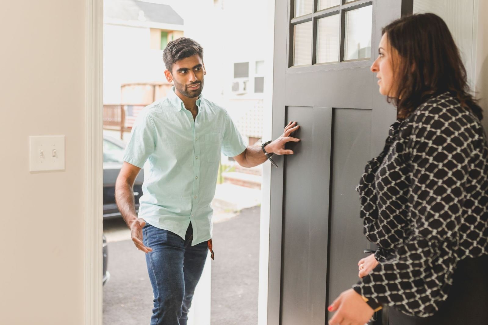 A man stands in an open doorway talking to a woman inside a house