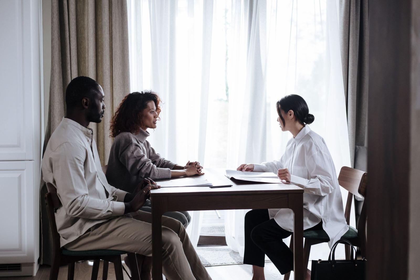 A couple sits at a table talking with a professional in a bright office