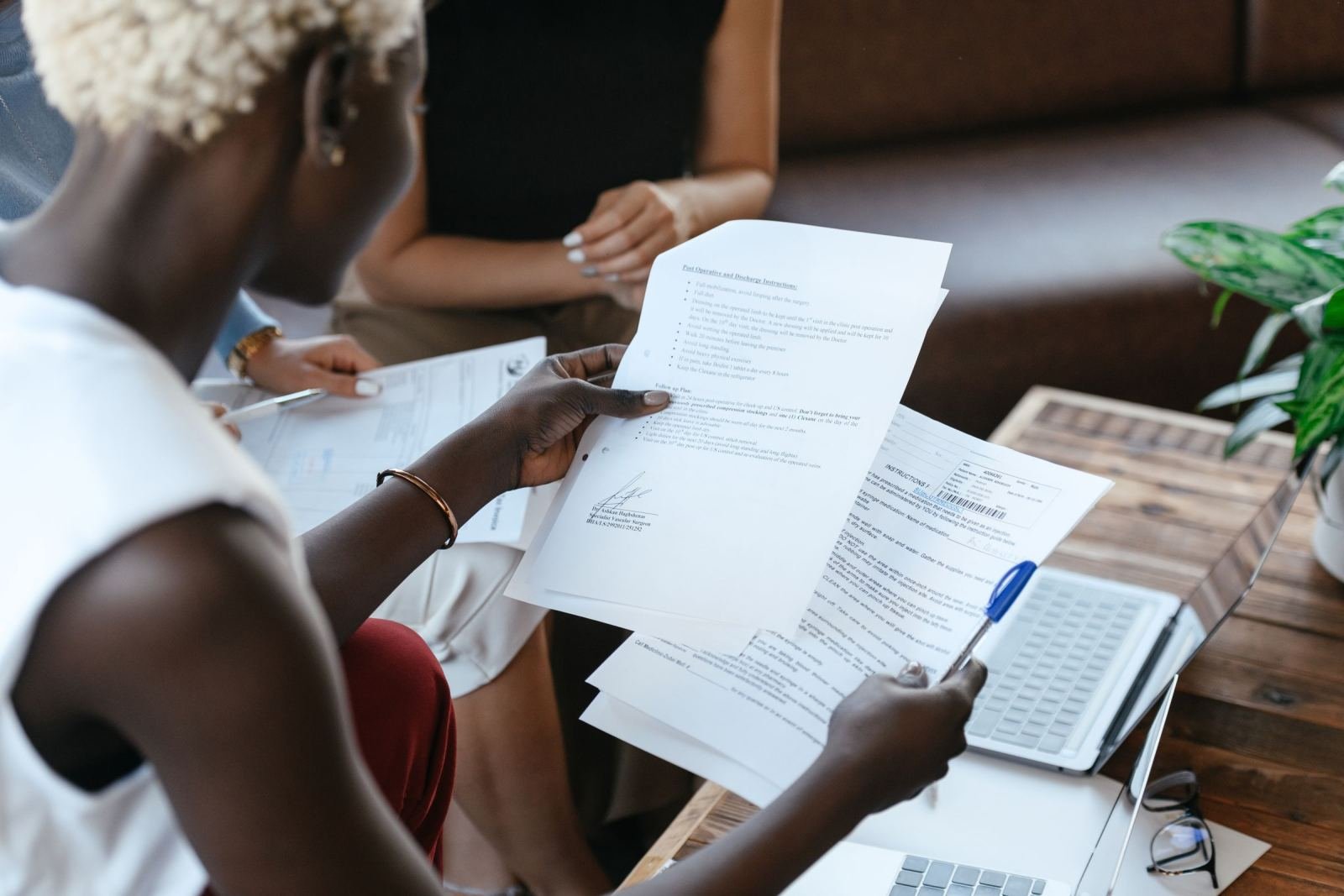 A person reviewing printed documents next to a laptop on a wooden table