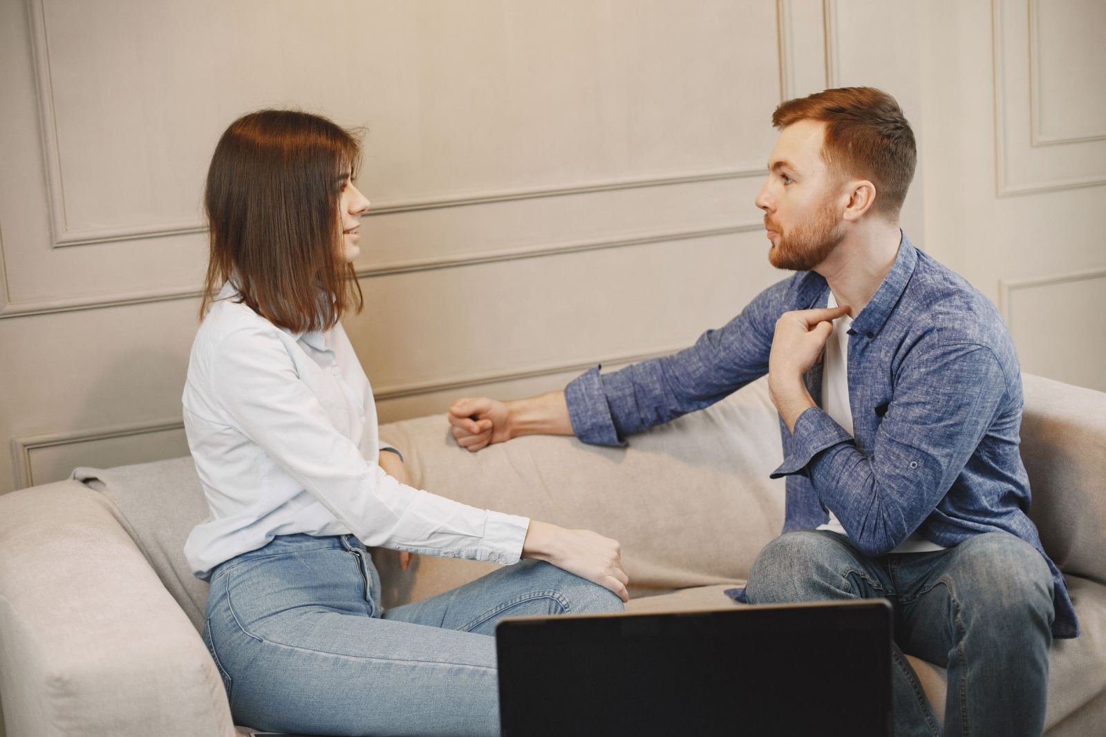 A man and a woman sit on a sofa and look at each other while talking