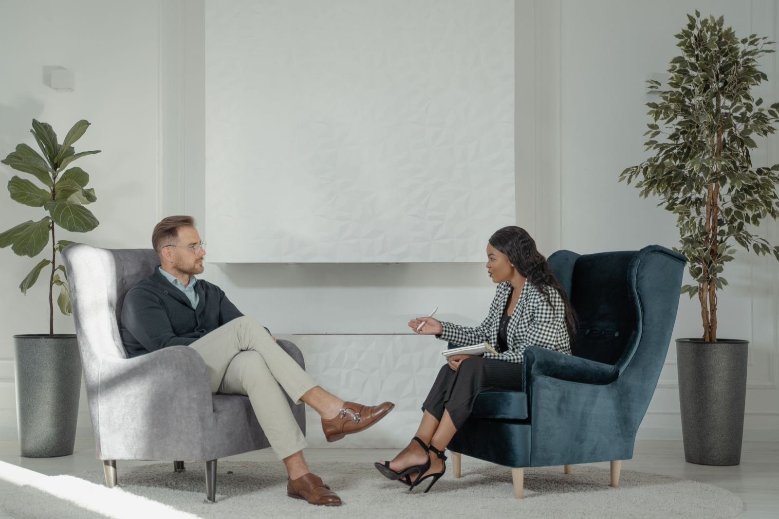 A bright, modern office shows a man and a woman talking while using a notebook.