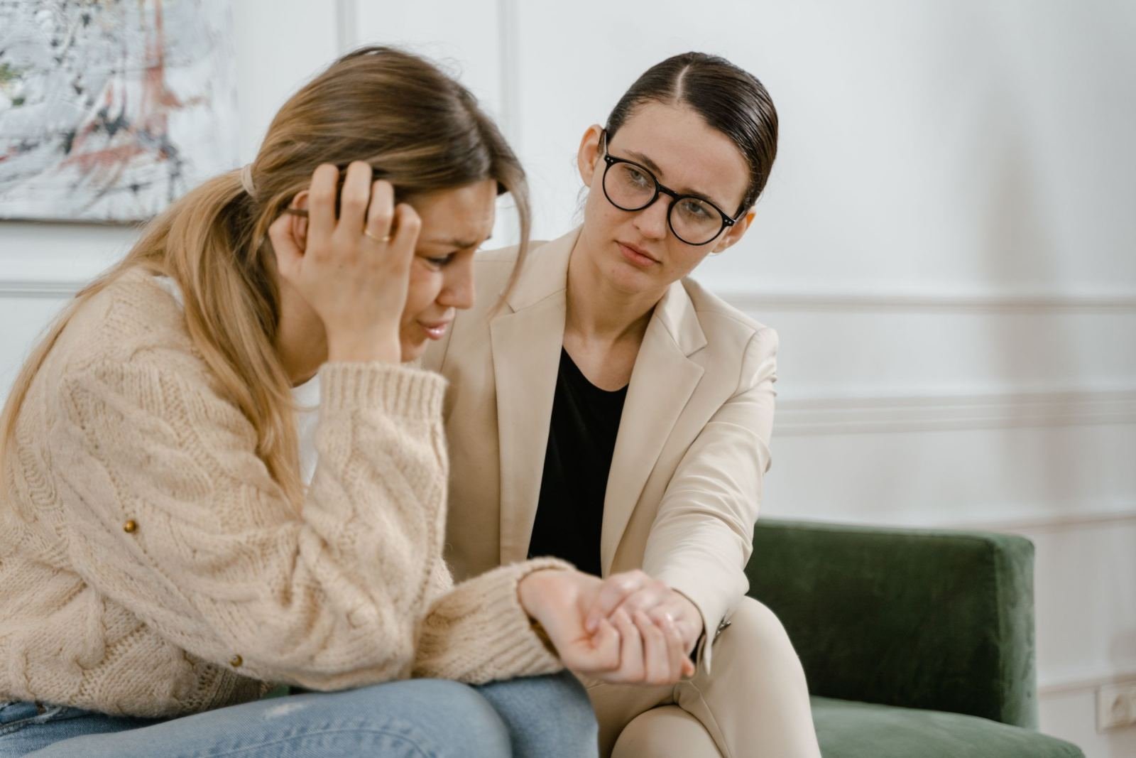 A counselor in a blazer holds the hand of a woman who is looking down with her head in her hand
