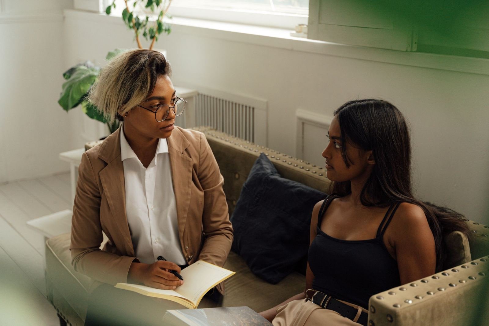 A professional woman with a notebook talks with a client on a couch