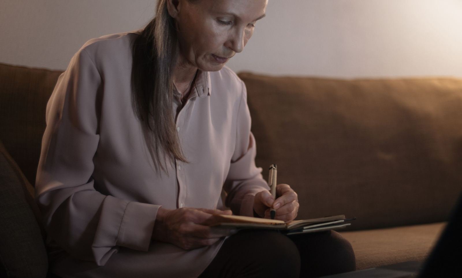 A woman sits on a sofa and writes in a notebook