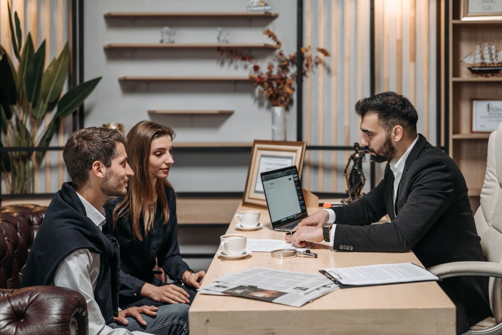 A couple meets with a professional in a suit at a desk with a laptop and papers