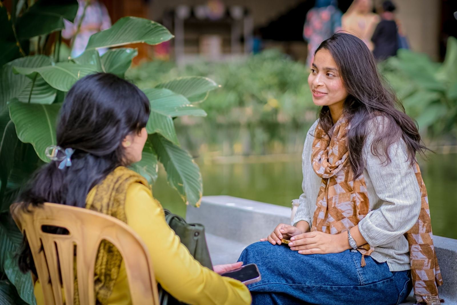 Two women talk together while sitting in an outdoor garden.