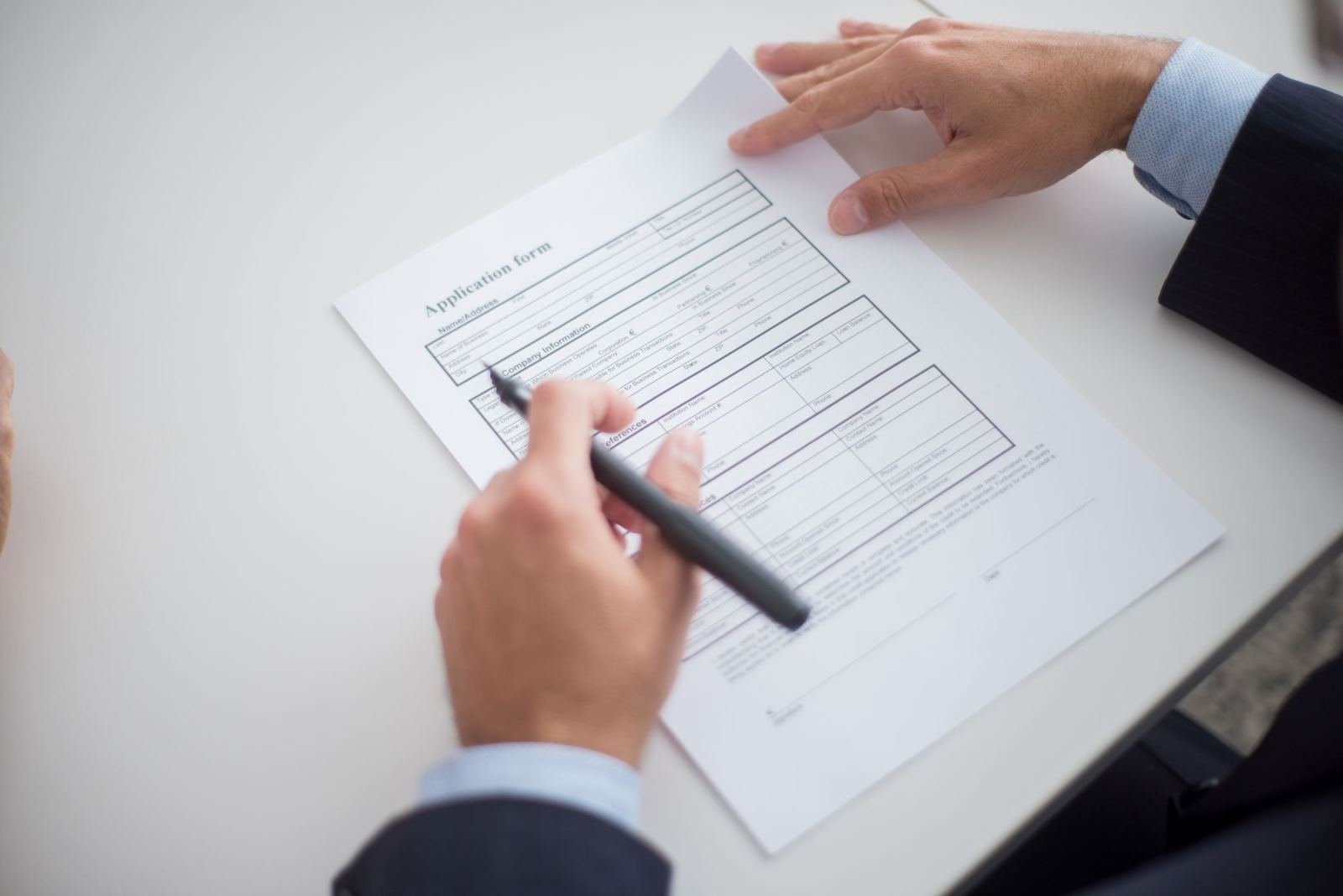 Two people in suits review a printed application form at a white desk