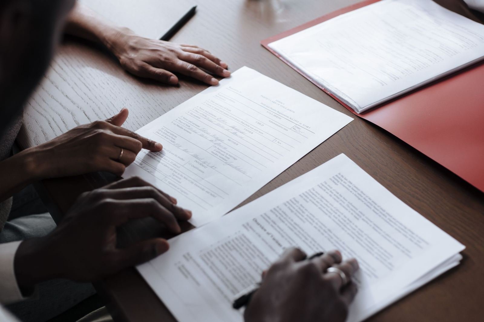 At a wooden table, two people look over printed papers and point out key parts.