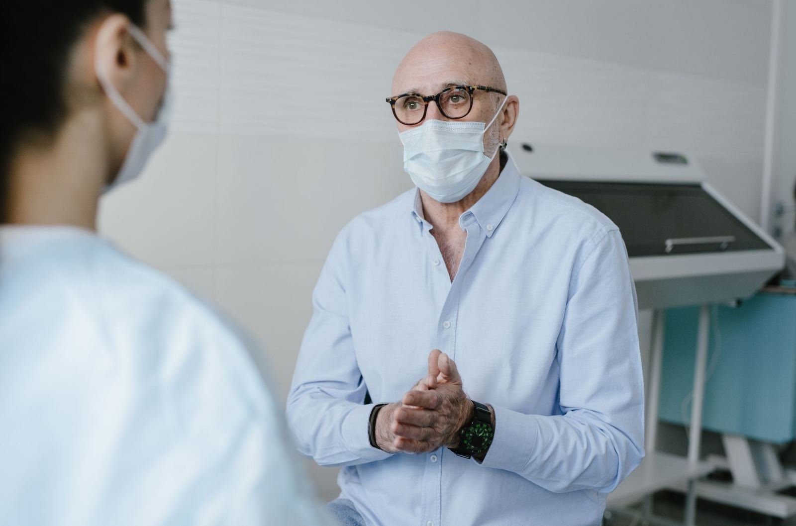 A man in a surgical mask talks to a healthcare provider in a clinic