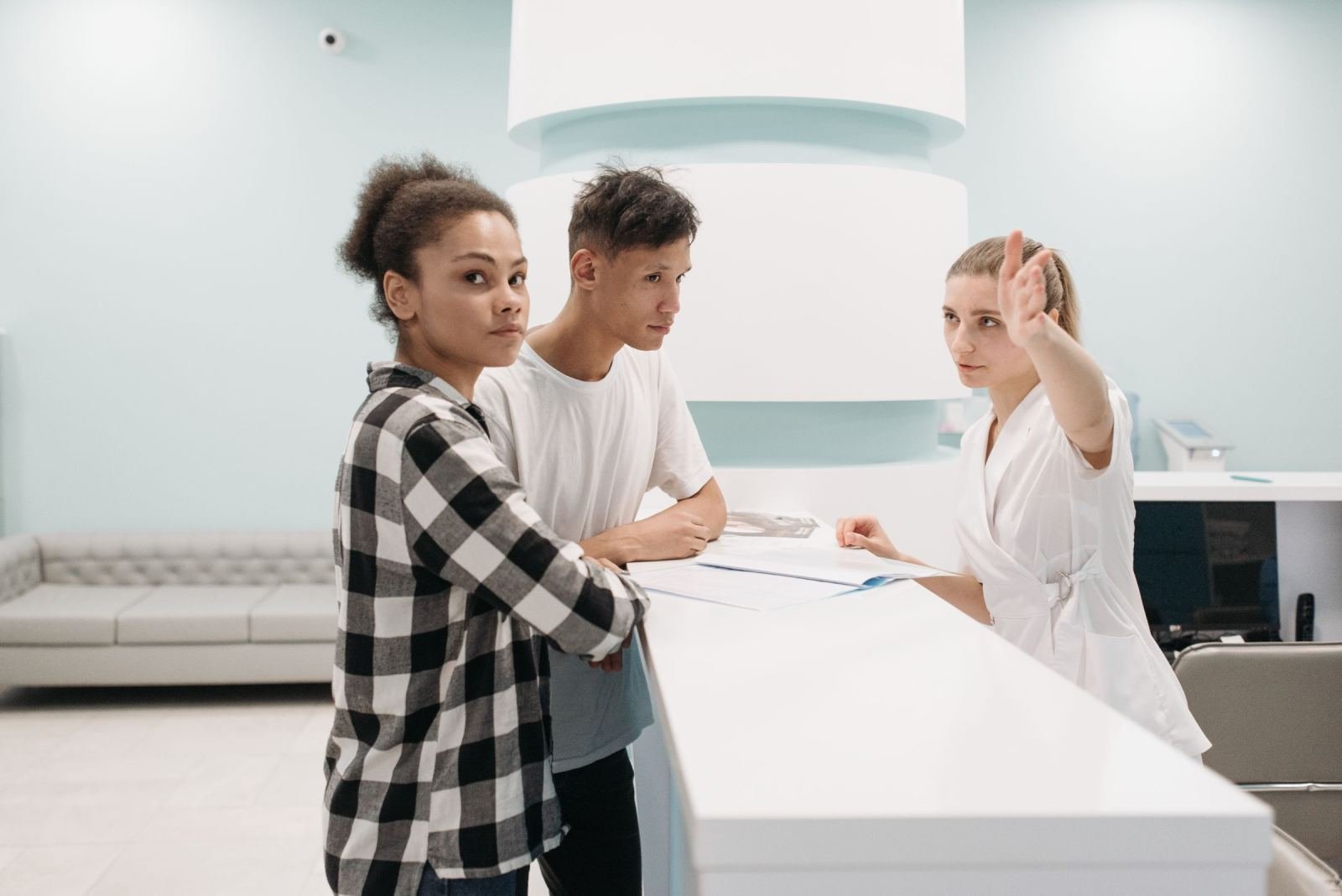 A clinic staff member in a white coat speaks with a couple at a reception desk